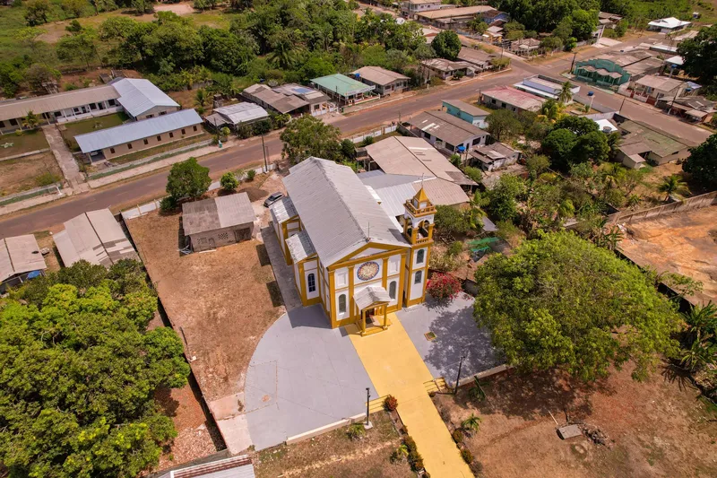 Vista aérea da Igreja Nossa Senhora de Nazaré, de telhado cinza e fachada amarela, com o adro e as ruas e casas ao redor