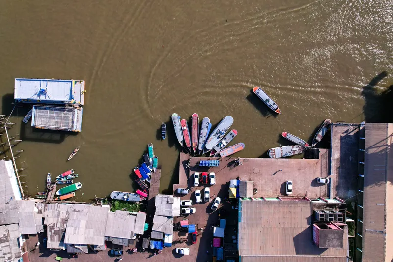 Vista aérea cenital del muelle de Santana con barcos en fila, estacionamiento con autos y galpones junto al río.