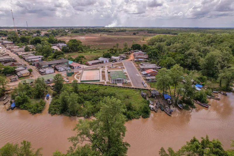 Vista aérea de la Praça Cabralzinho con su cancha, junto al río fangoso donde hay barcas amarradas, rodeada de casas y bosque