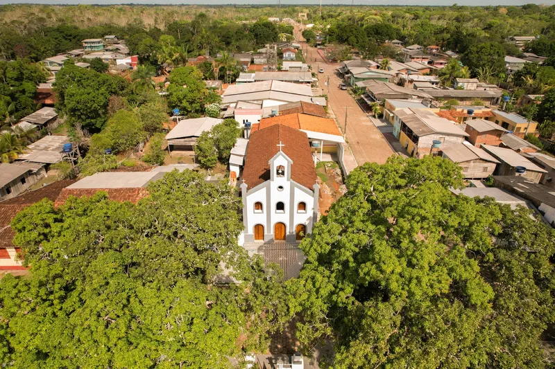 Aerial view of Igreja Nossa Senhora da Assunção among treetops, with the houses and streets of Mazagão Velho around it.