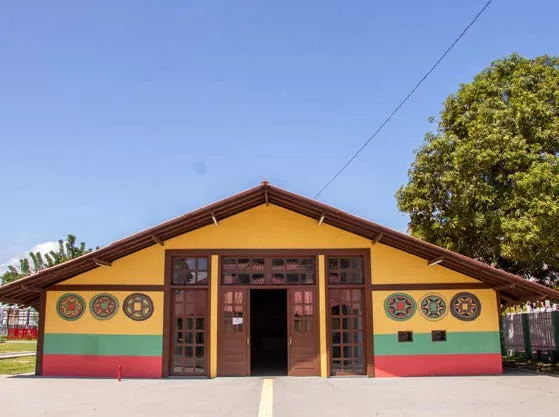 Fachada amarela, verde e vermelha do Centro de Cultura Negra, com porta de madeira e árvore ao lado.