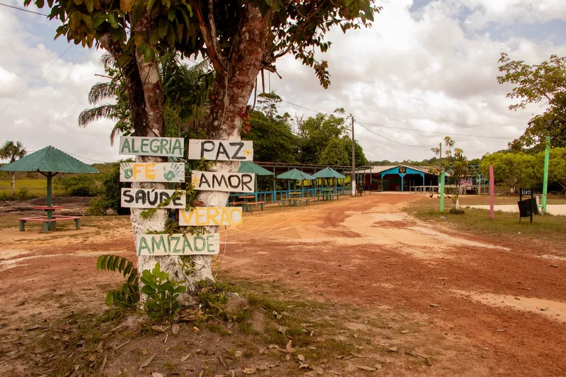 Entrance to Balneário Asa Aberta: a tree with painted signs (joy, peace, love, faith), a red dirt road and colourful kiosks in the background