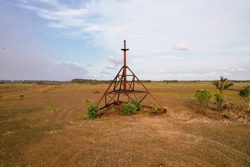 Structure métallique rouillée en forme de pyramide dans la plaine de la base aéronavale d'Amapá, entourée d'arbustes sous un ciel légèrement nuageux