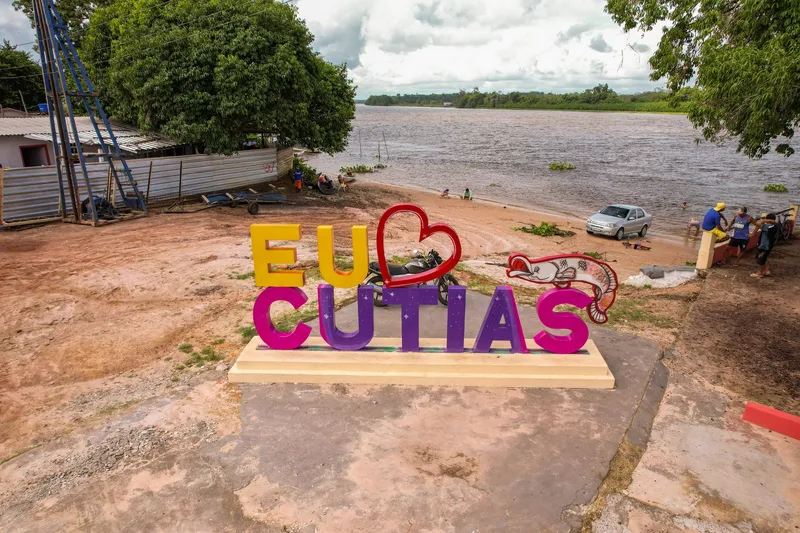 Enseigne colorée « Eu ♥ Cutias » ornée d'un poisson sur le front de rivière de Cutias do Araguari, avec le large fleuve et la forêt en face