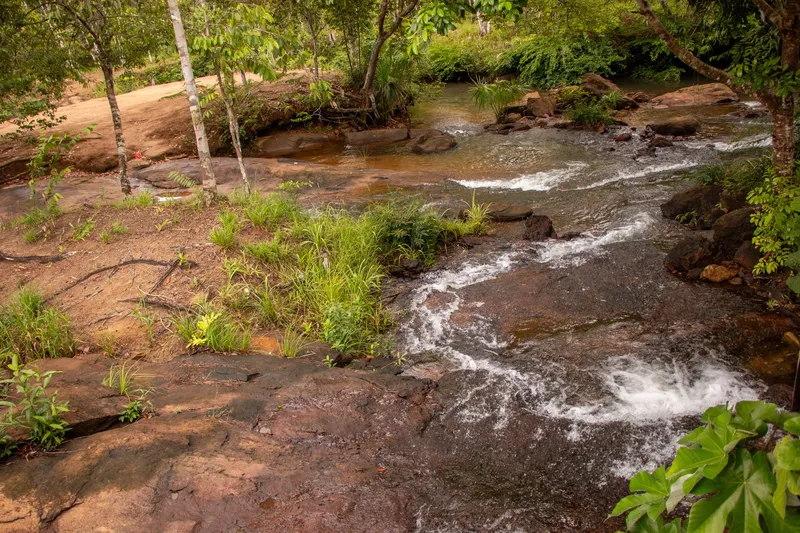 Rapids at Cachoeira do Traíra running over reddish rocks, with grass and trees on the bank