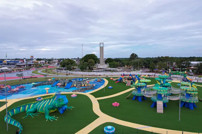 Juegos temáticos del Parque Meio do Mundo: iguana gigante, árboles estilizados con pasarelas y zona acuática azul, con un obelisco al fondo.