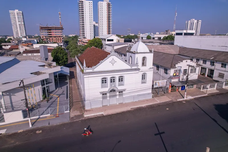 Vista aérea lateral da Igreja Matriz de São José de Macapá, branca com telhado de telhas, entre casarões e prédios altos.