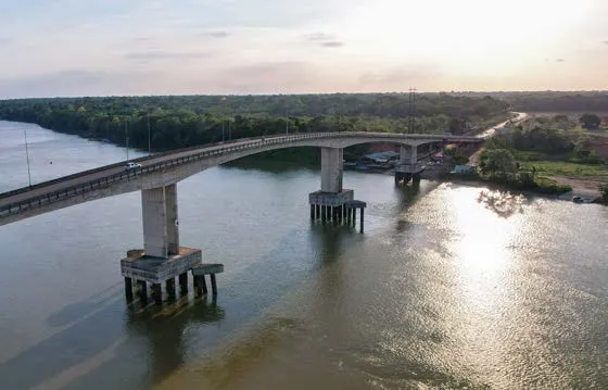 Aerial view of the bridge over the Matapi River, with concrete piers, wooded banks and sunlight on the water.