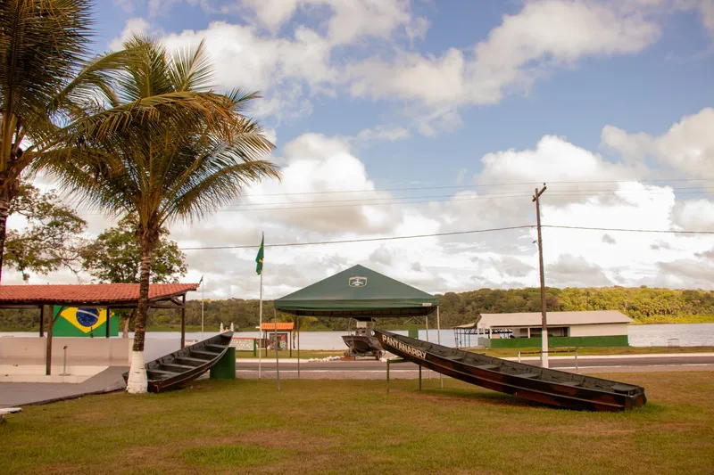 Canoas de madera expuestas en el césped de Clevelândia do Norte, con carpa verde, palmeras y el río Oiapoque al fondo.
