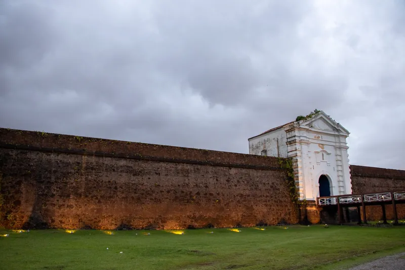 Muralha de pedra da Fortaleza de São José de Macapá iluminada ao entardecer, com o portal branco e a ponte de acesso.