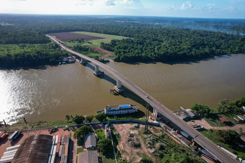 Aerial view of the Ponte da Integração over the Matapi River, with a moored boat, a container yard and forest across.