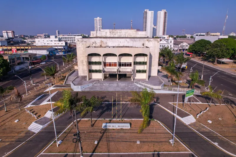 Vista aérea frontal do Teatro das Bacabeiras, em Macapá: prédio de concreto com arcos, praça com palmeiras à frente e prédios altos ao fundo.