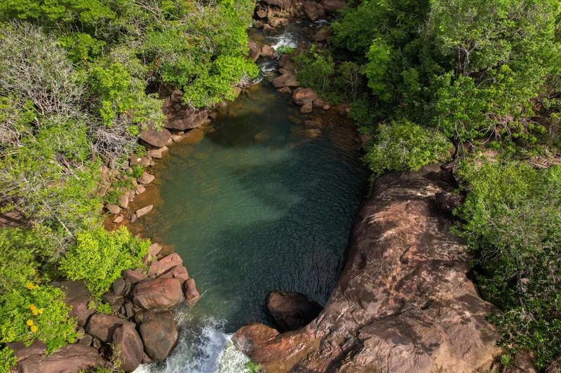 Poza de agua verde y transparente en la Cachoeira do Pium vista desde arriba, entre lajas de piedra y vegetación, con pequeña caída en primer plano