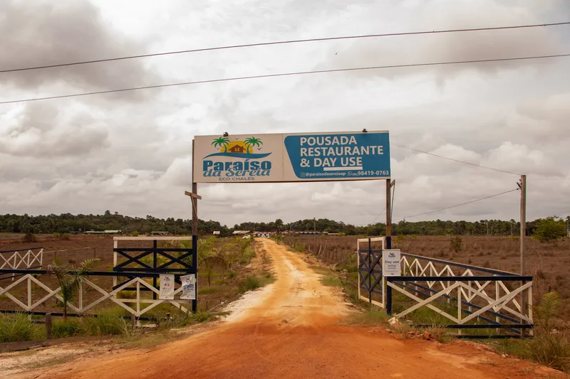 Entrance arch of Paraíso da Sereia over a dirt road, with white fences and cloudy sky