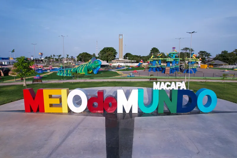Letrero colorido "Meio do Mundo Macapá" en la entrada del Parque Meio do Mundo, con juegos gigantes y un obelisco al fondo, al atardecer.