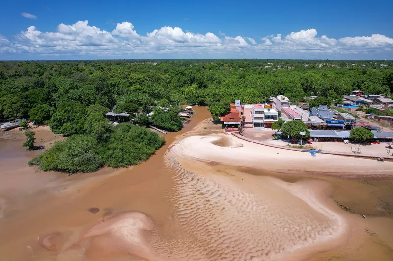 Vue aérienne de l'entrée de la rivière Paxicu avec bancs de sable à marée basse, forêt dense et front de mer de Fazendinha à droite, sous ciel bleu.