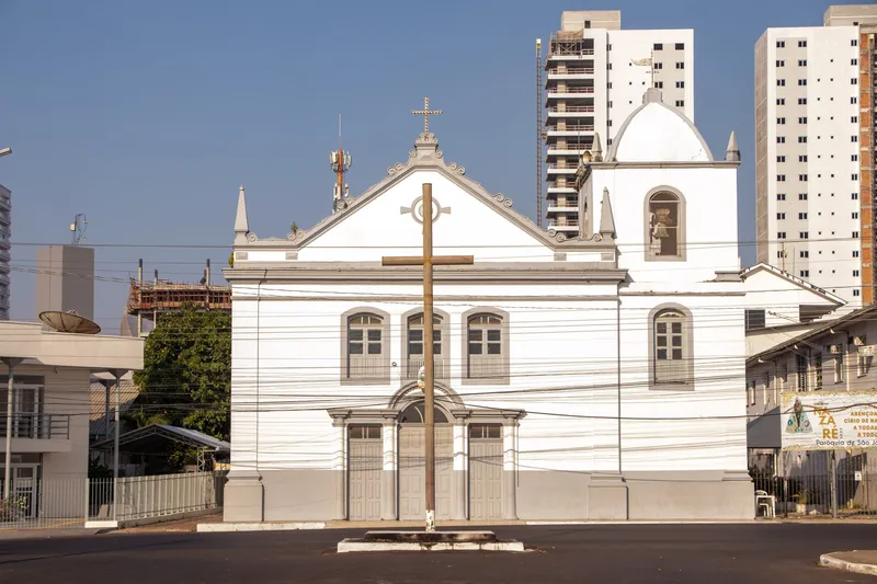 Igreja Matriz de São José de Macapá vista de frente, com grande cruz de madeira na praça e prédios altos ao fundo.