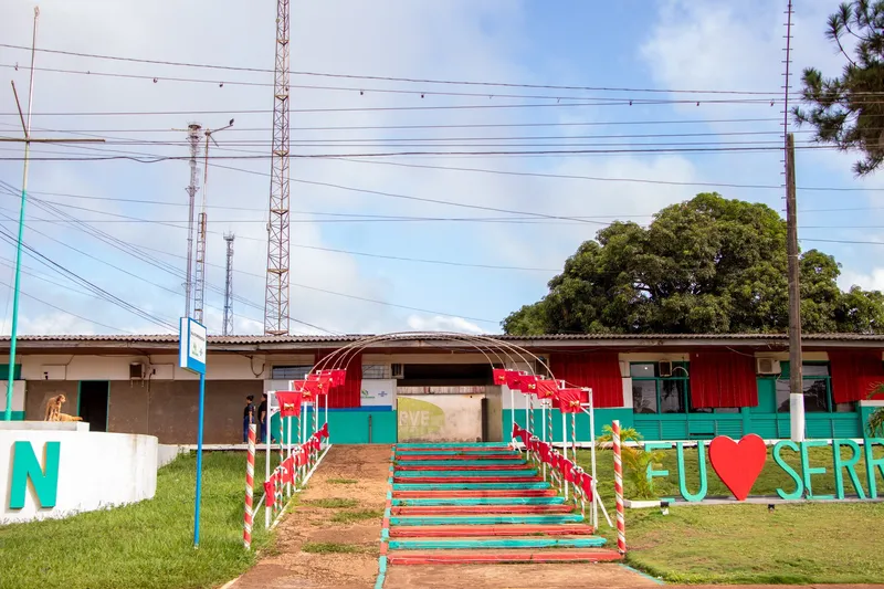 Escadaria colorida em vermelho e verde decorada com arco e bandeirolas, levando a prédio baixo; ao lado, letreiro "Eu amo Serra" com coração vermelho.