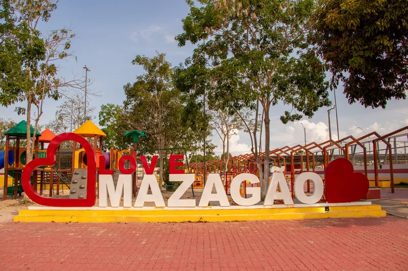 Love Mazagão sign with red hearts in the Mazagão Novo square, with a colorful playground and trees behind.