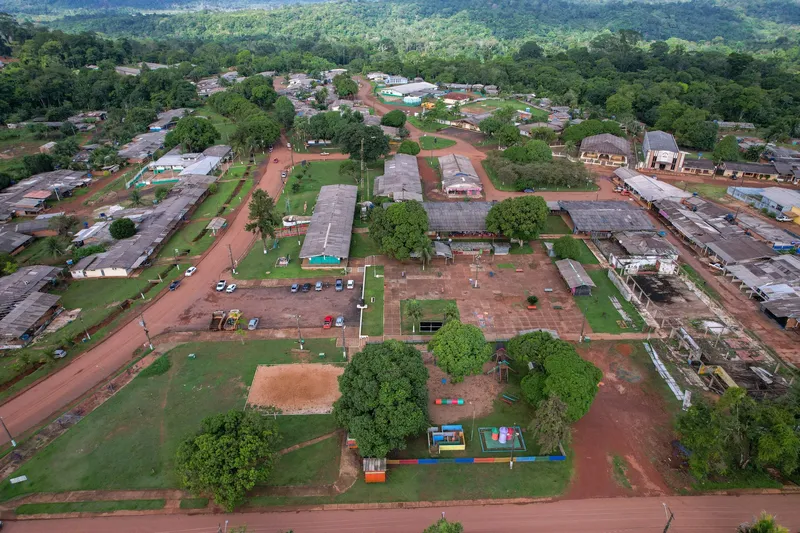 Vista aérea da Vila Serra do Navio com galpões, casas, gramados, parquinho infantil e estacionamento, tendo a floresta ao fundo.