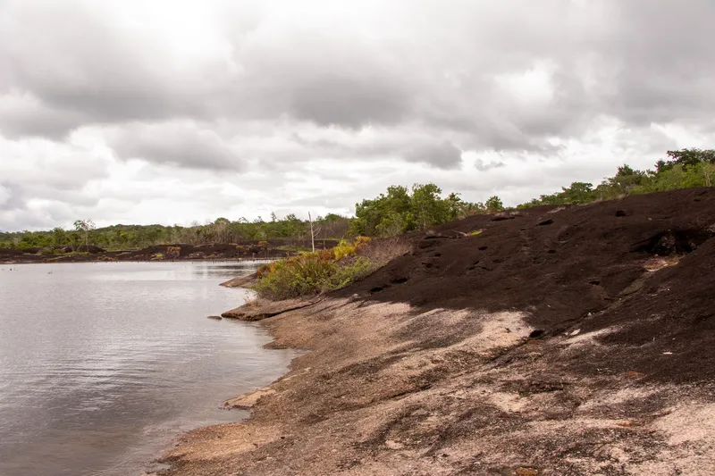 Orilla rocosa de la Cidade das Pedras que baja hasta las aguas tranquilas del río Araguari, con vegetación baja y cielo cargado