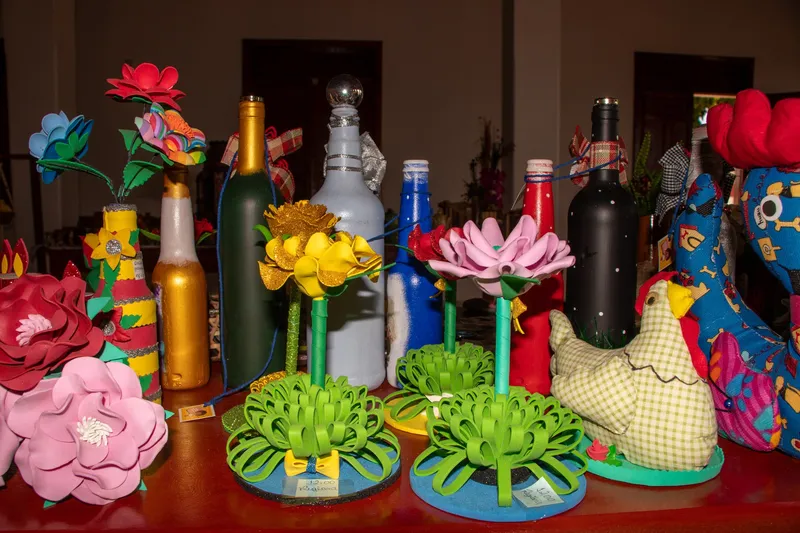 Colorful handicrafts at Casa do Artesão de Mazagão: decorated bottles, foam flowers and fabric hens on a table.