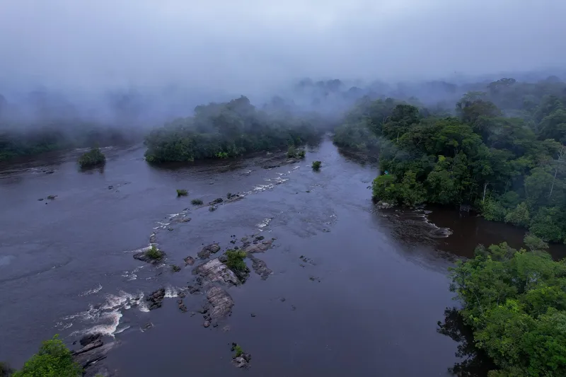 Vista aérea de un río ancho con piedras y rápidos entre islas de selva, bajo neblina, en el Parque Nacional Montanhas do Tumucumaque.