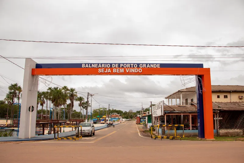 Pórtico naranja y azul con el texto Balneário de Porto Grande, Seja bem-vindo (bienvenido) sobre la calle de entrada, con palmeras a la izquierda