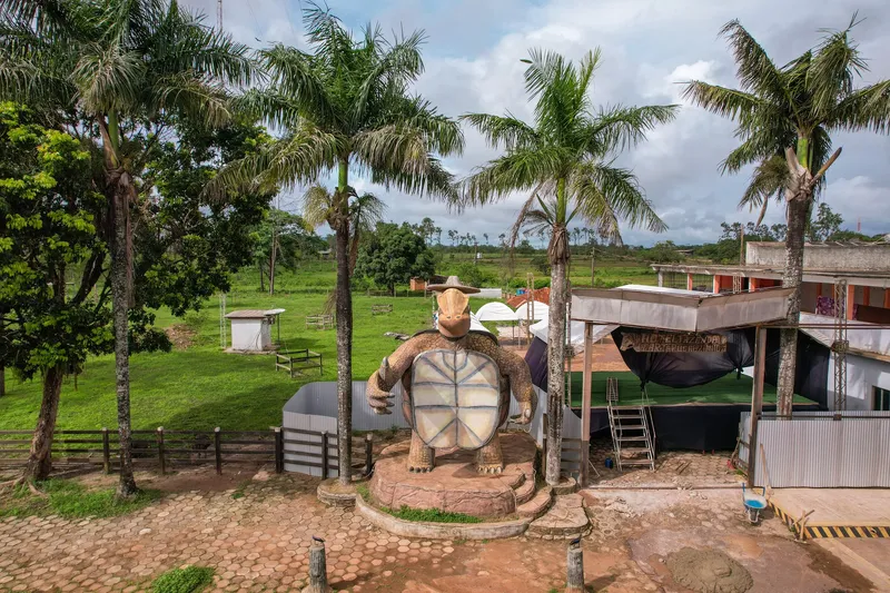 Vista elevada del Monumento da Tartaruga entre palmeras, con suelo adoquinado, un escenario al lado y campo verde al fondo.