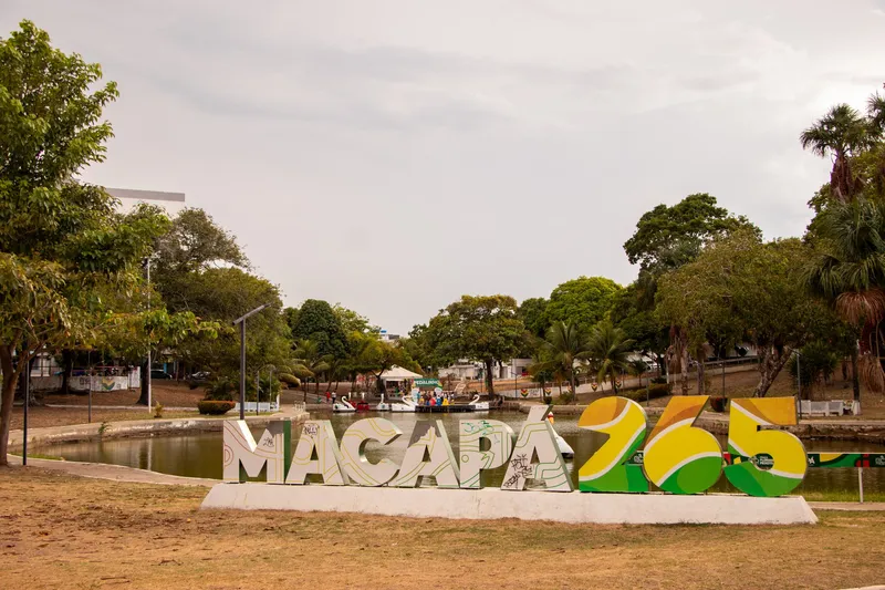 Letreiro "Macapá 265" diante do lago da Praça Floriano Peixoto, com pedalinhos em forma de cisne e árvores ao fundo, em dia nublado.