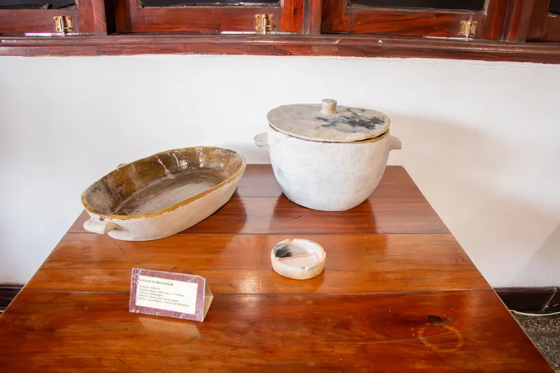 Louças de barro claro (travessa oval, panela com tampa e pequena tigela) expostas sobre mesa de madeira com placa no Museu de Arqueologia e Etnologia.