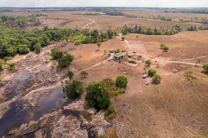 Vue aérienne des rapides du Topéca : lit rocheux à l'eau sombre à gauche, forêt riveraine et petite ferme avec maisons et enclos dans la savane sèche