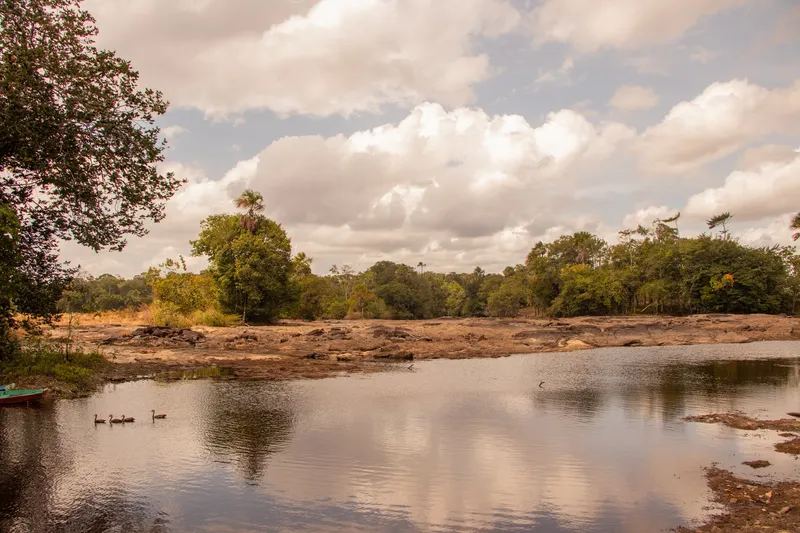 Large plan d'eau des rapides du Topéca reflétant les nuages, avec des oiseaux qui nagent, des dalles rocheuses et la forêt sur l'autre rive
