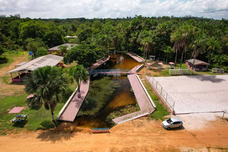 Vista aérea do Balneário Sagrado Coração de Maria: igarapé com deques e ponte, quiosques, quadra de areia e palmeiras ao redor