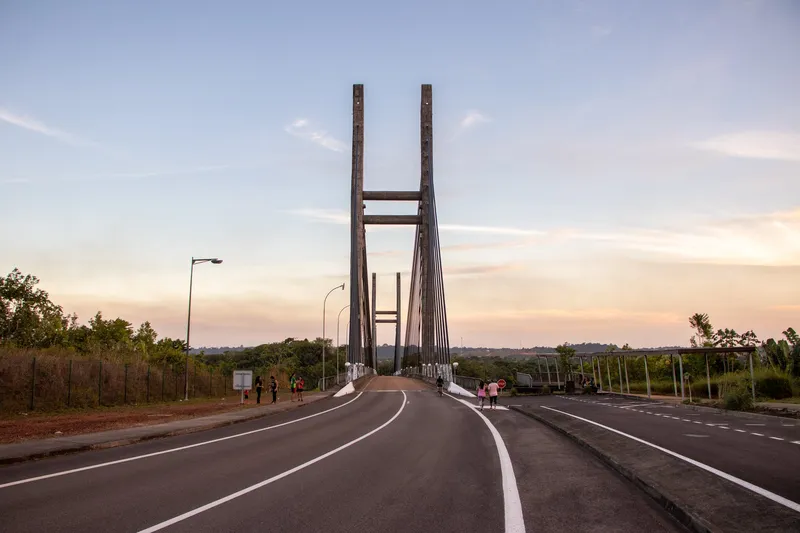 Access road to the Binational Bridge at dusk, with the towers ahead and small figures of people walking on the shoulder