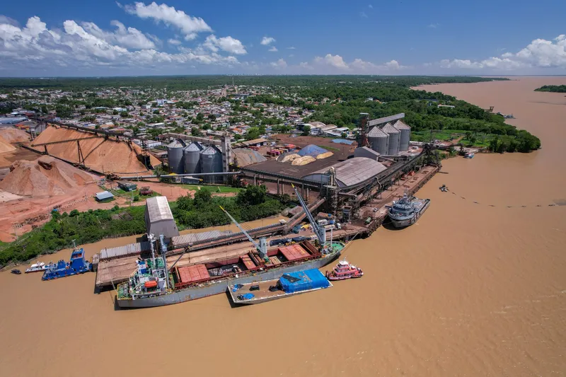 Vista aérea de las Docas de Santana: silos, cintas transportadoras y pilas de astillas de madera, con un buque de carga atracado.