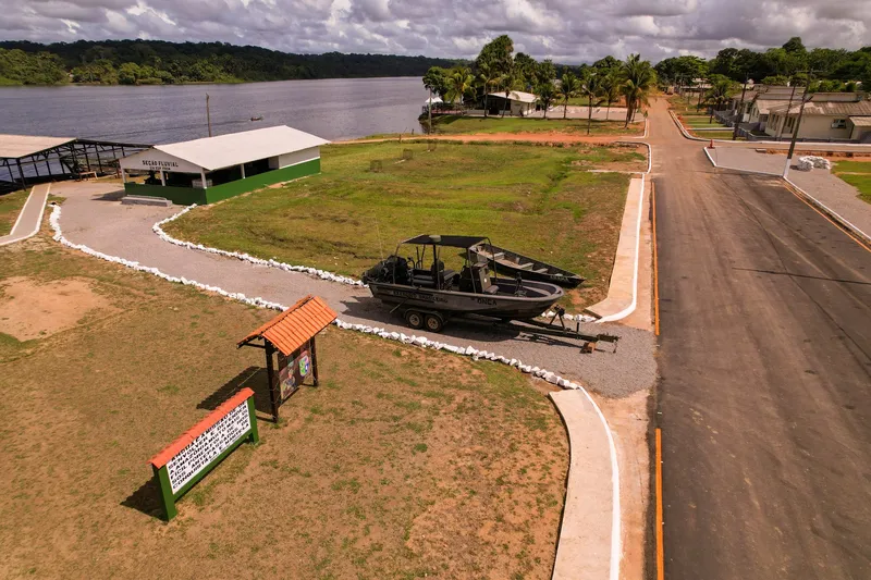 Vista aérea de Clevelândia do Norte con lancha militar expuesta en el césped, galpón verde y blanco, calle y el río Oiapoque al fondo.