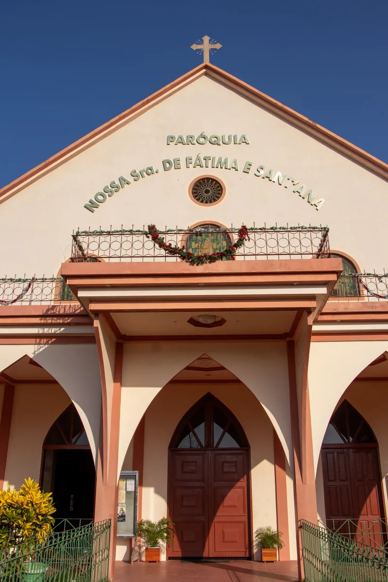 Detalhe da fachada da Paróquia Nossa Senhora de Fátima e Sant'Ana: letreiro, rosácea, sacada e porta de madeira em arco.