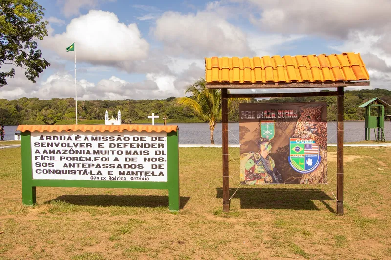 Placas con una frase sobre la Amazonia y panel militar en Clevelândia do Norte, con el río Oiapoque, la iglesia y la selva al fondo.