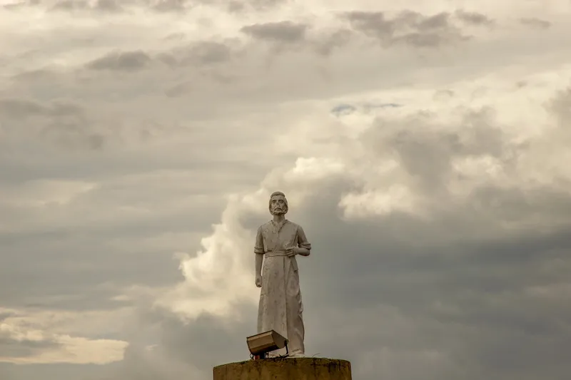 Detalhe da imagem branca de São José no alto da Pedra do Guindaste, com um refletor aos pés e céu de nuvens carregadas ao fundo.