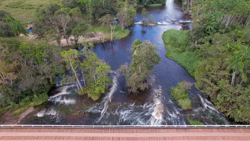 Vista aérea sobre el puente de madera del Balneário Água Fria, con rápidos blancos entre islotes de árboles y el río al fondo