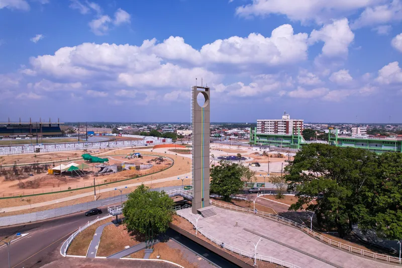 Vista aérea do Marco Zero do Equador: torre com abertura circular, praça e árvores, com o Estádio Zerão à esquerda ao fundo.