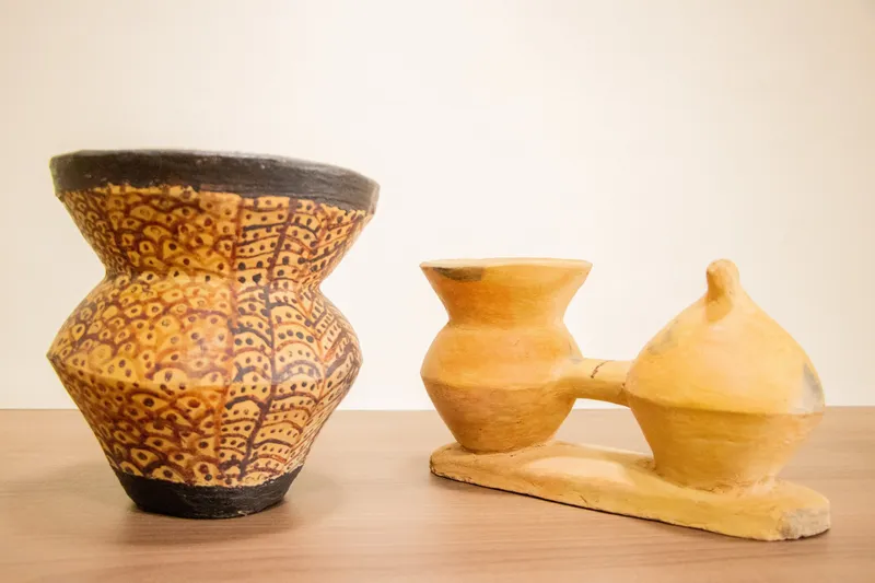 Piezas de cerámica indígena expuestas en el Museo Kuahí: un jarrón pintado con grafismos y un recipiente doble amarillo sobre una base