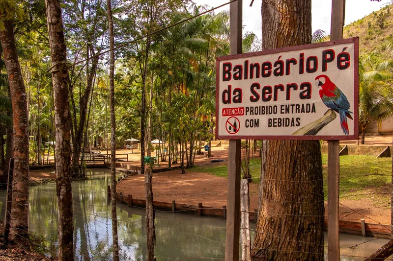 Placa do Balneário Pé da Serra com desenho de arara, ao lado do igarapé e da área com quiosques