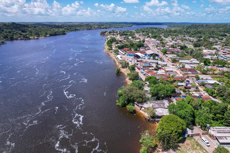 Vista aérea diurna da cidade à beira do rio largo, com corredeiras, casas e ruas ao longo da margem