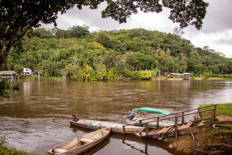 Wooden boats moored at a small pier on the Amapari River, with houses and a forested hill behind.