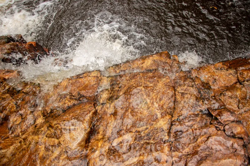 Detalle de agua espumosa sobre piedra anaranjada en la pequeña caída del Balneário da Dona Antônia.