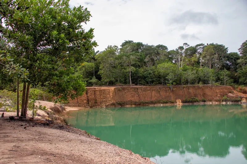 Green-water lake at Barranco do Geraldão, with an orange earth bank, forest reflected behind and a tree on the shore