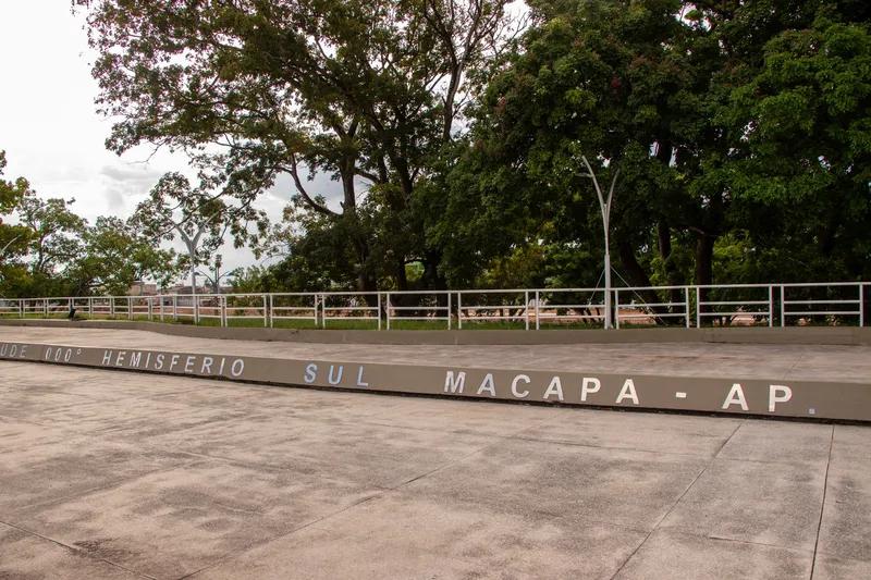 Inscrição "Hemisfério Sul, Macapá, AP" na mureta da praça do Marco Zero do Equador, com árvores ao fundo.
