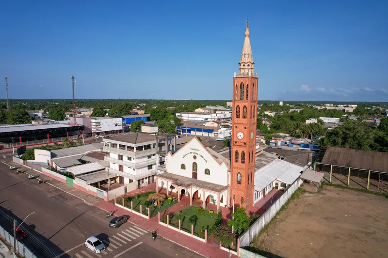Vista aérea da Igreja Nossa Senhora de Fátima e Sant'Ana, com torre alta de tijolos e relógio, ao lado de uma avenida.